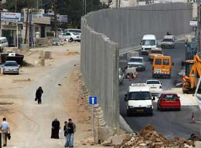 Palestinians walk next to part of the Israeli security barrier in the West Bank town of Ram February 20, 2005. An expected Israeli cabinet vote on Sunday, the endorsement of a barrier route looping around Jewish settlement blocs in the West Bank, added to Palestinians' fears Israel was cementing its grip on large swathes of territory they also seek. [Reuters]