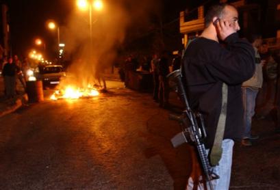 A Palestinian gunman, member of Al Aqsa Martyrs' Brigades uses his mobile phone next to a burning tire closing the street in the West Bank city of Ramallah Thursday, March 31, 2005. A group of Palestinian militants fired Wednesday at Palestinian leader Mahmoud Abbas' West Bank headquarters while he was in the compound, but he was not injured, security officials said. (AP Photo/Nasser Nasser) 