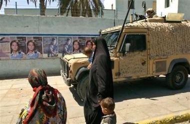 An Iraqi woman with children walks past the posters encouraging Iraqis to vote for the new constitution in a national referendum on Oct. 15, as a British soldier holds his position on a vehicle roof, in southern city of Basra, 550 kilometers (340 miles) from Baghdad, Sunday, Aug. 21, 2005. 