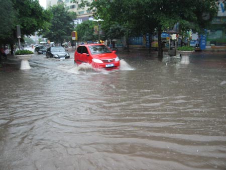 Vehicles drive down a flooded street after a heavy downpour in Southwest China's Chongqing Municipality, July 17, 2007. [Xinhua]